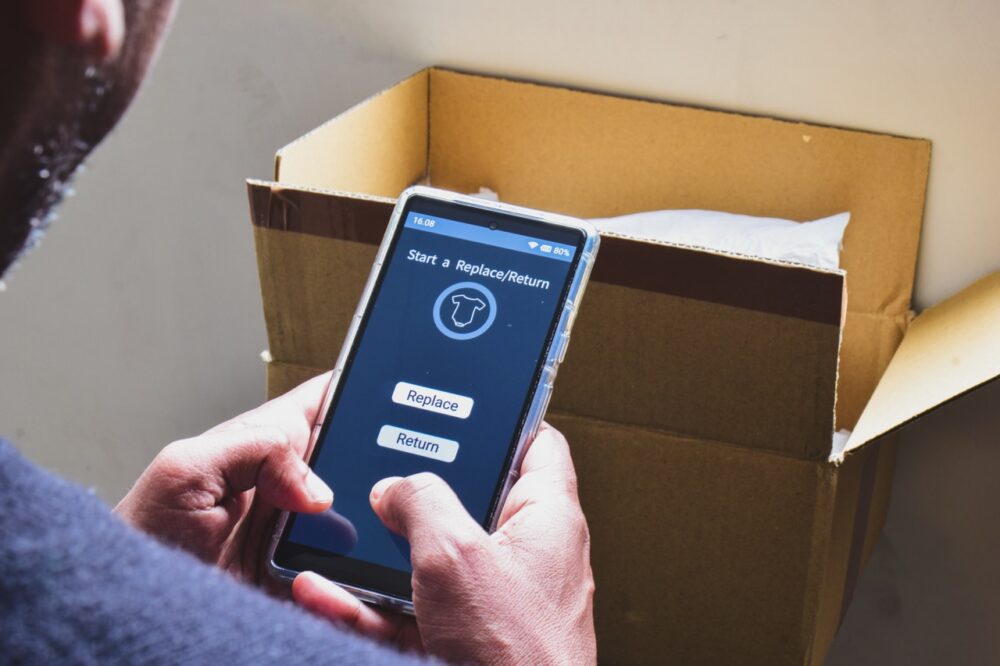 A South Asian man started the process to return a product purchased online. E-commerce, selective focus on the smartphone screen.