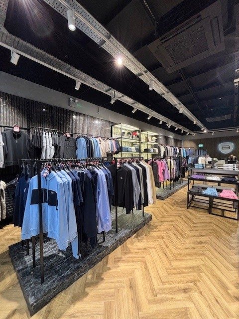 Designer menswear store interior with rails of jackets and knitwear on dark marble-effect plinths, herringbone wood flooring and track lighting