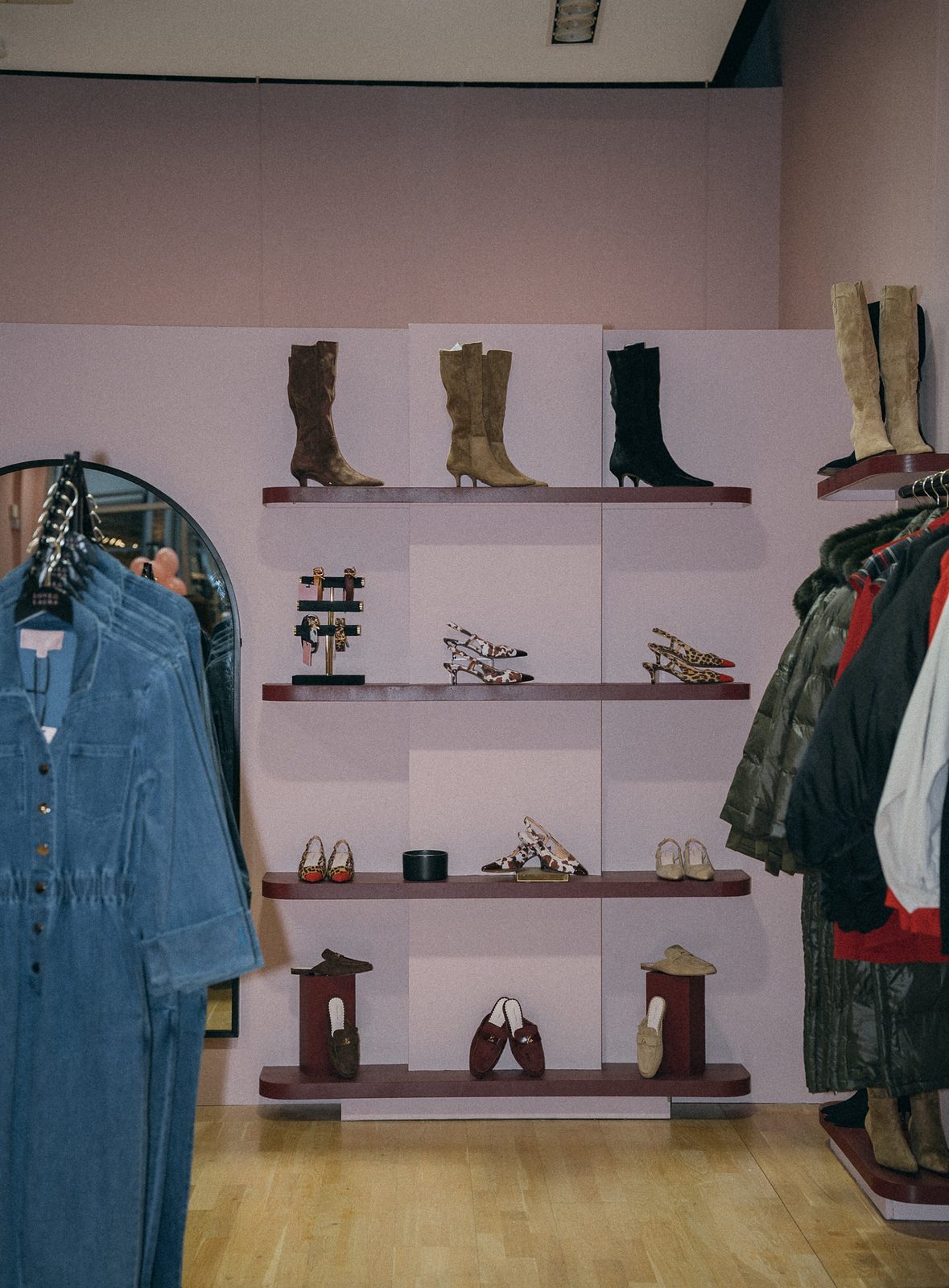 Love Laura shoe wall with suede knee-high boots, slingbacks and loafers on burgundy shelves, beside rails of denim and coats