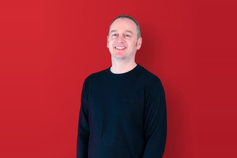 Nikk Smith, Sales Director at Pixel Inspiration, smiling against a red background